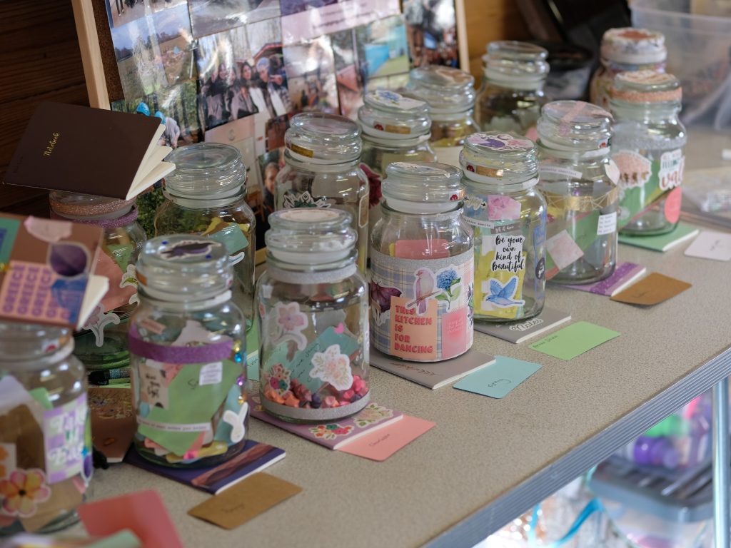 Jars and notebooks arranged on a table. The glass jars contain lots of colourful items.