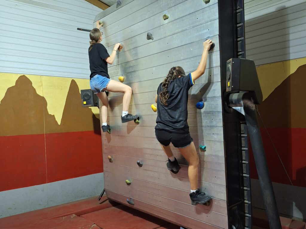 Two girls half way up a climbing wall.