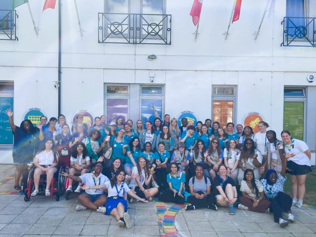 A large group of girls and young women sitting and standing in front of a white stone building.